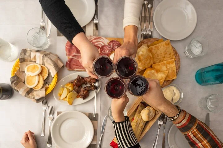 Four people raising glasses of red wine over a table of cured meats, fried dough, bread and small plates, seen from above
