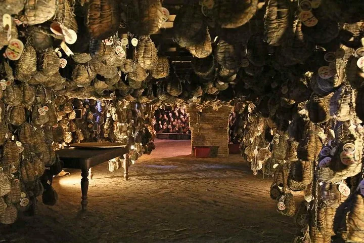 A dim cellar with hundreds of tagged, string-tied cured meats hanging from the ceiling around a wooden table