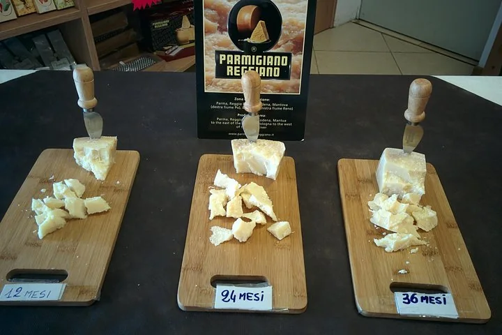 Three bamboo boards of broken Parmigiano Reggiano with cheese knives, labelled 12, 24 and 36 mesi
