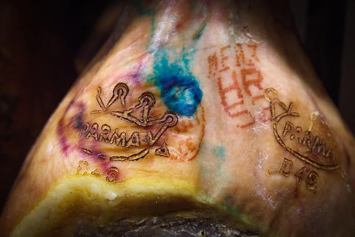 The rind of a whole ham stamped with two crown brands reading PARMA and coloured inspection marks